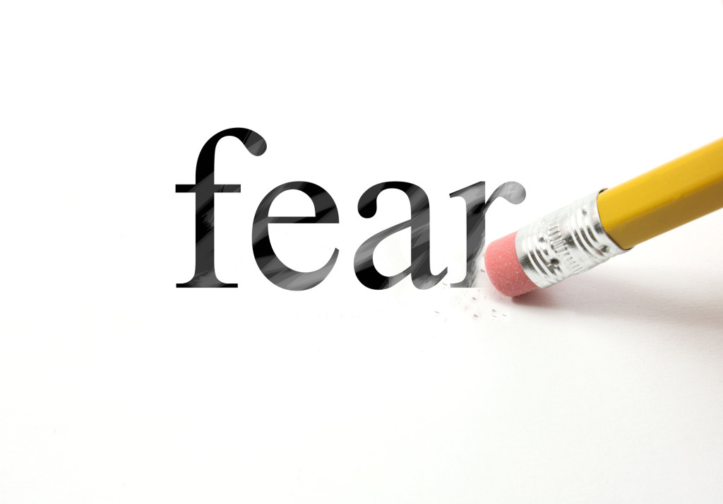 The word Fear written with a pencil on white paper.  An eraser from a pencil is starting to erase the word fear.